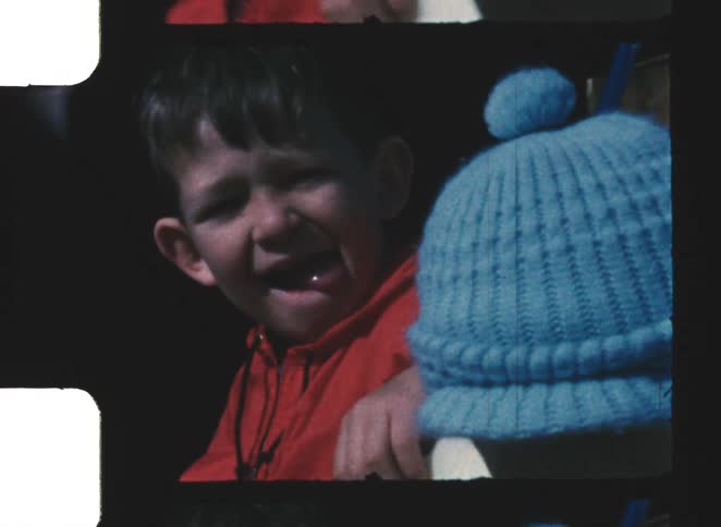 Two children side by side one wearing a red jacket and the other a blue hat seated close together