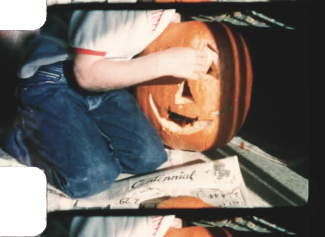A boy sitting next to a carved pumpkin