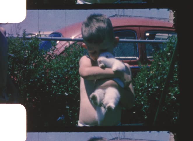 A young boy holds his pet rabbit while standing outdoors on a sunny summer day