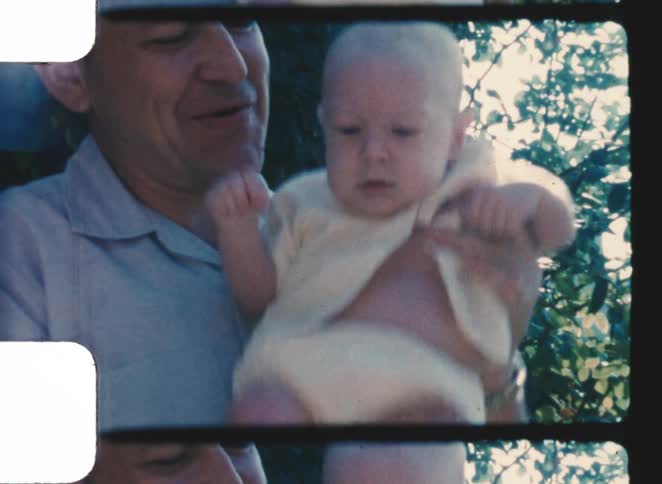 The man raises his infant son up and smiles