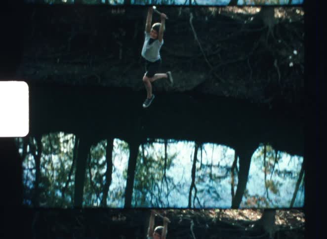 Person swinging on a rope above still water surrounded by trees
