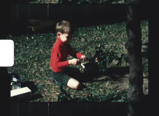 Boy sits on the grass holding a branch in a shaded outdoor area