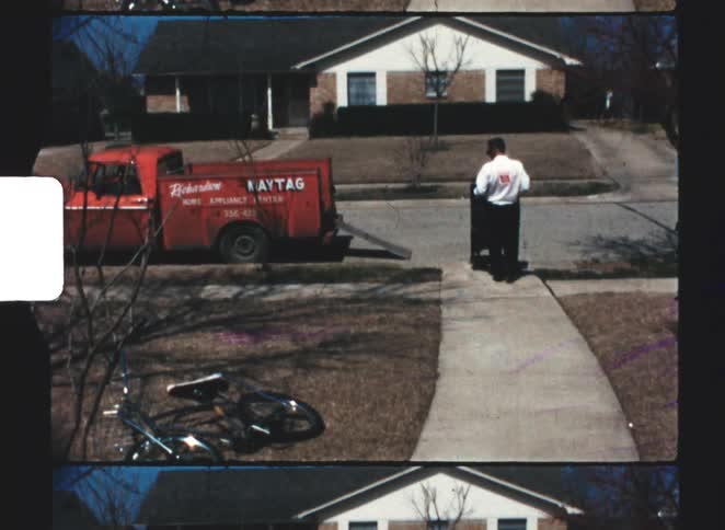 Man maneuvers an appliance along a sidewalk while delivering to a house during the daytime