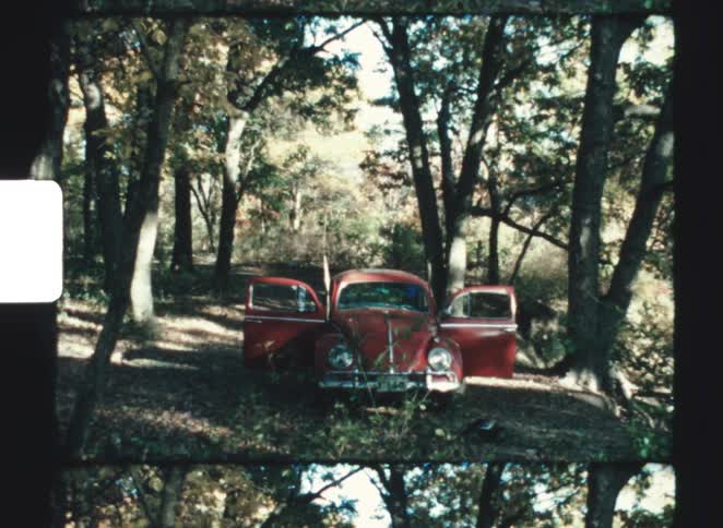 A vintage red car parked with open doors in a quiet forest