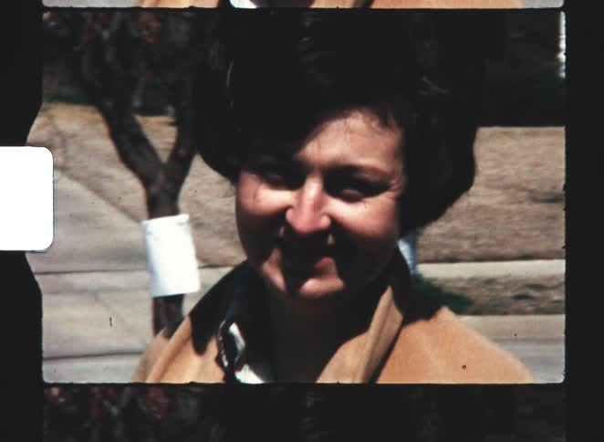 A young woman wearing a brown jacket with short fluffy hair smiling outdoors under the sun