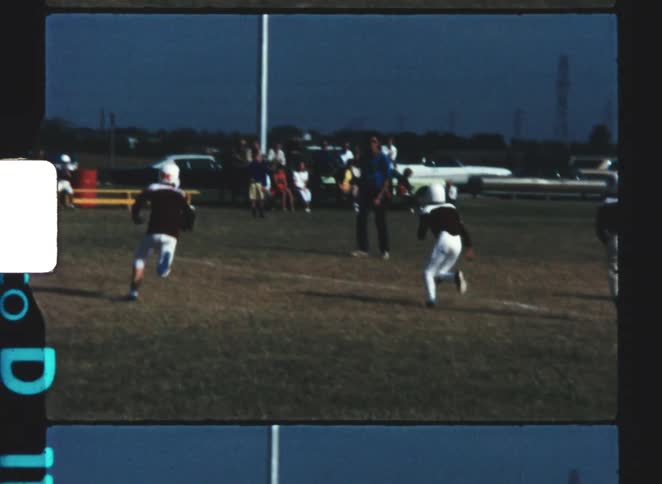 Youth players practicing american football on an open field with parked cars in the background