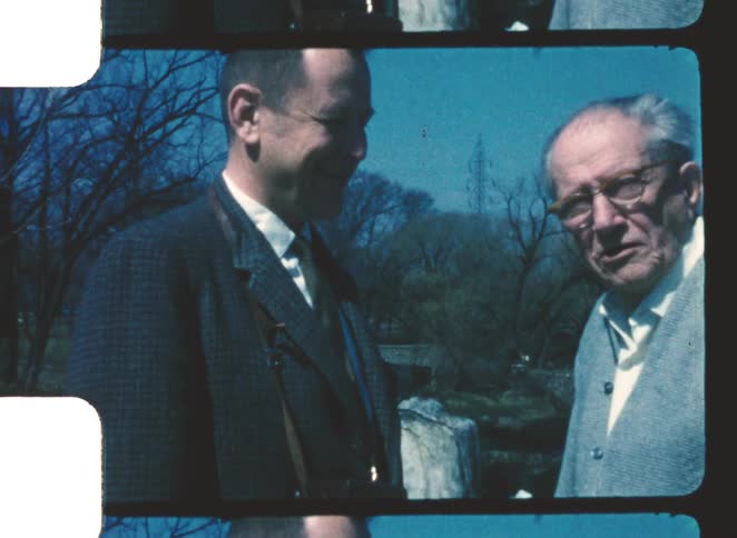 Two men standing outdoors in front of leafless trees