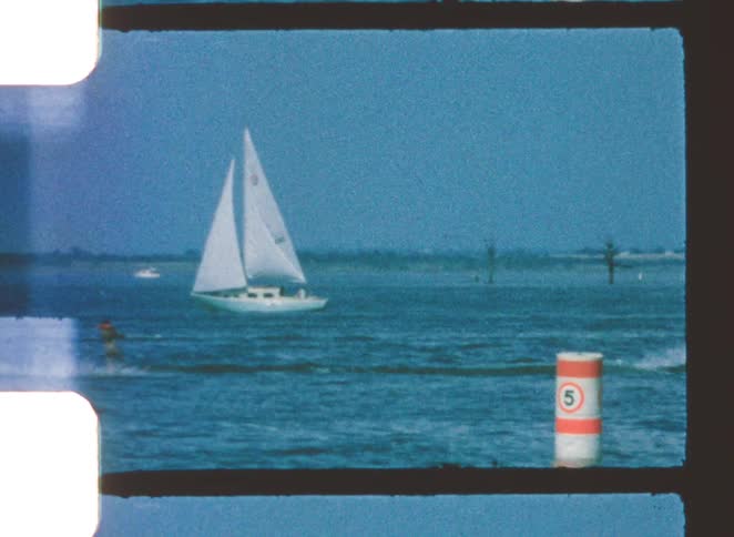 A person surfing across the ocean while being pulled by a boat at midday with other sailboats passing by