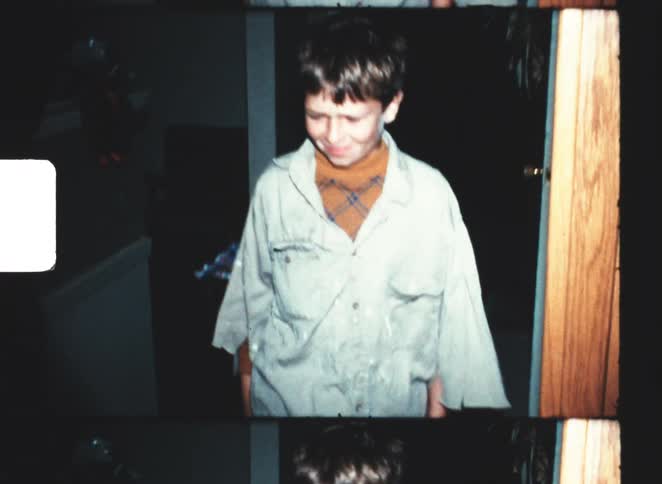 Boy wearing oversized ragged clothes walks down the hall in a dimly lit home