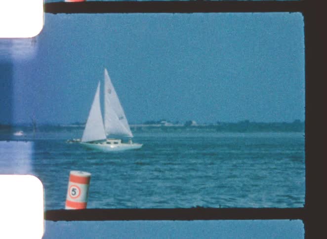 Whitehulled sailboat moves across open waters with a navigation buoy visible in the foreground