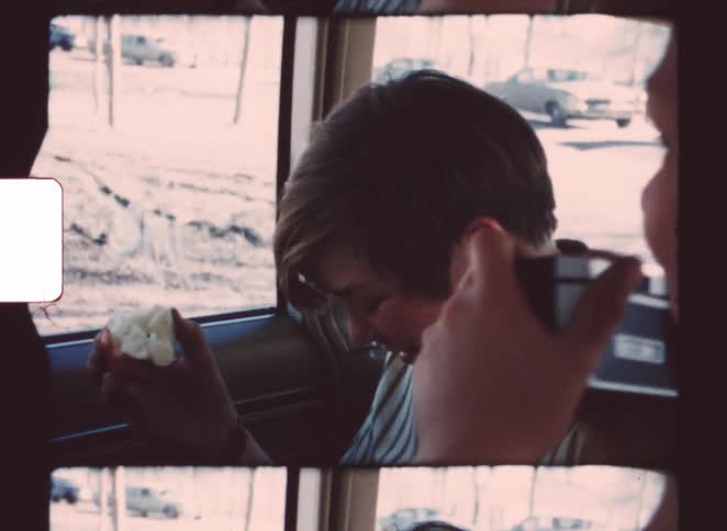 A group of children taking pictures on the backseat of a car with a winter background visible through the window
