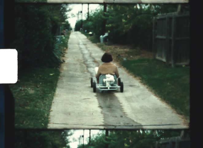 Child riding a pedal cart along a narrow path between fences