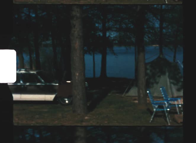 A camping with a tent and chairs next to a car in the middle of the forest
