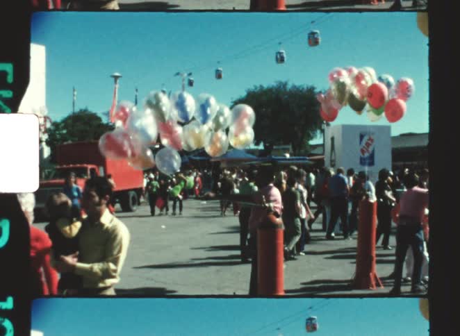 Crowd walking through an outdoor event area with vendors selling colorful balloons