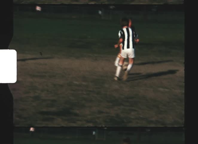 A lot of young soccer players some in a black and white striped jersey and the other ones in a yellow top running and kicking a soccer ball across a dirt and grass field during a game