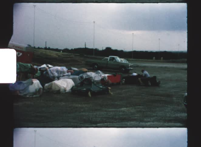 Covered items spread across an open area with parked vehicles in the background