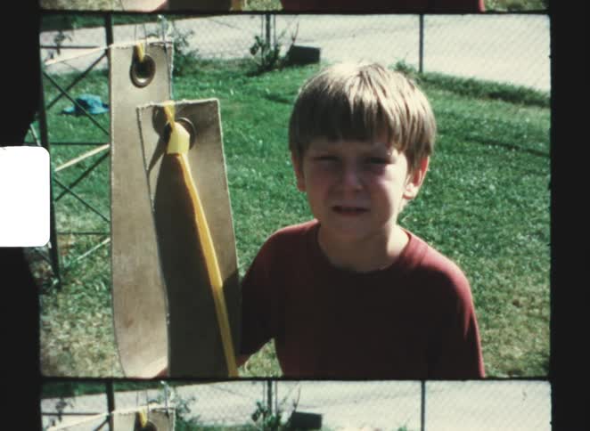 Child standing beside a swing secured with a yellow strap in a grassy area