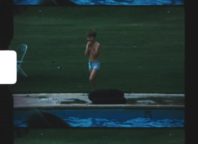 A kid in blue shorts walking beside the pool at midday