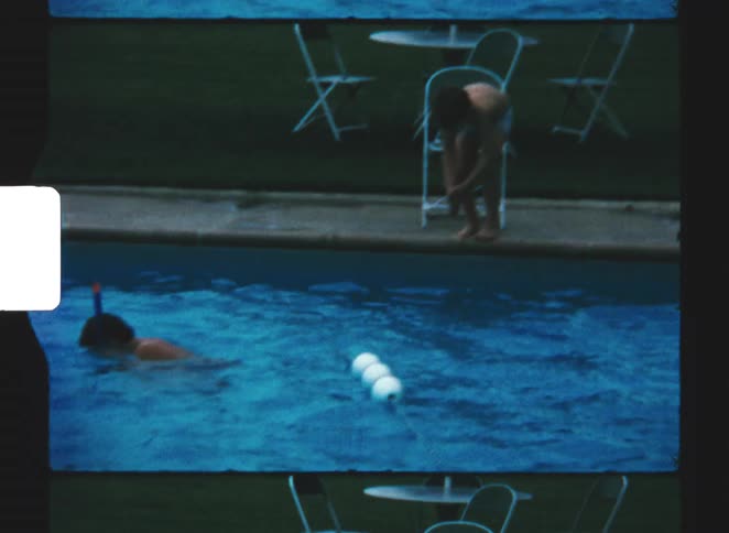 A kid wearing only swim trunks jumping into an outdoor pool at midday with another kid already in the water swimming