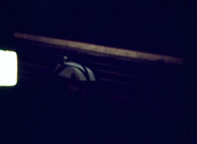 Vintage footage from inside a dark amusement park ride shows an iconic bobsled vehicle traveling up a steep lift hill its white shell glowing faintly in the deep shadows