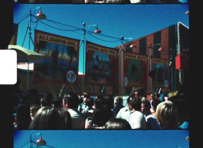 Crowd watches fair attractions with colorful banners under blue sky and red lamps