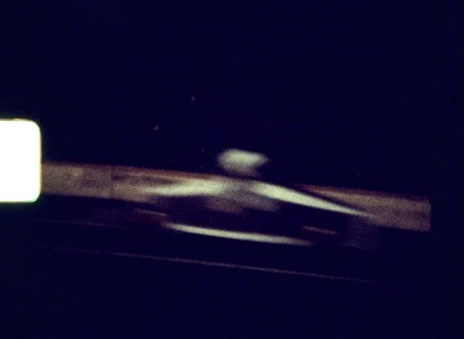 Two men race side by side in small vintage open wheel race cars on a dark track at night