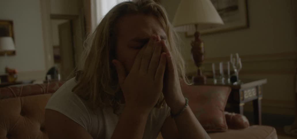 A man sits on a couch running his hands through his hair and over his face