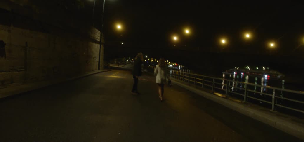 A man and woman playfully walk along a waterfront at night