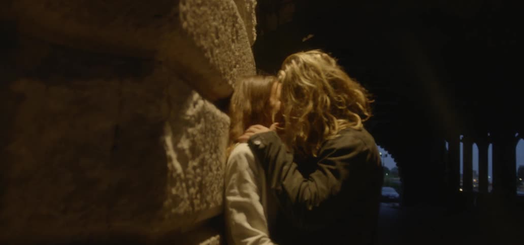 A man and woman make out against a building wall