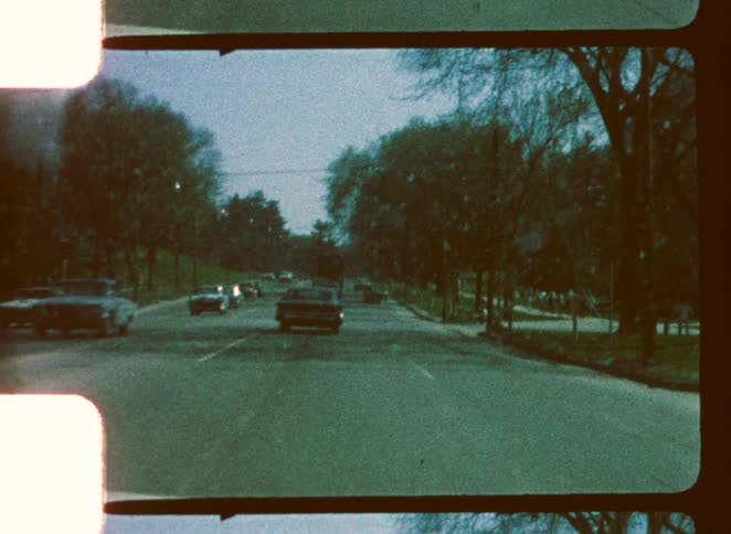 Some cars driving in a tarmac road with white stripes on the center with trees around