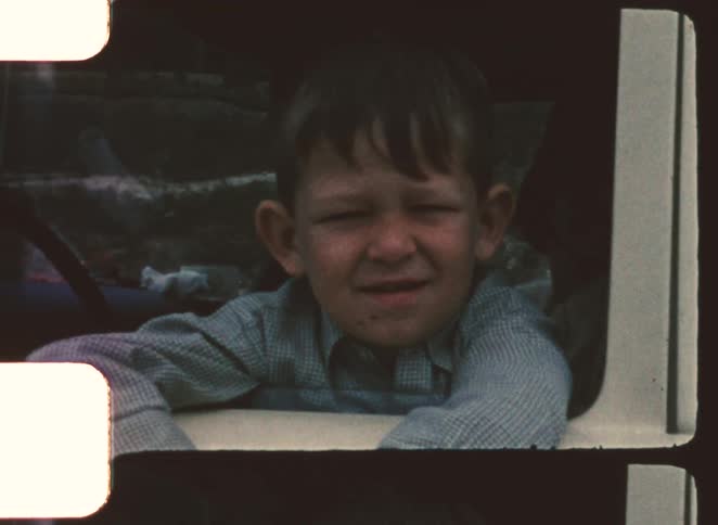 Closeup of a young boy squinting while leaning against a window frame