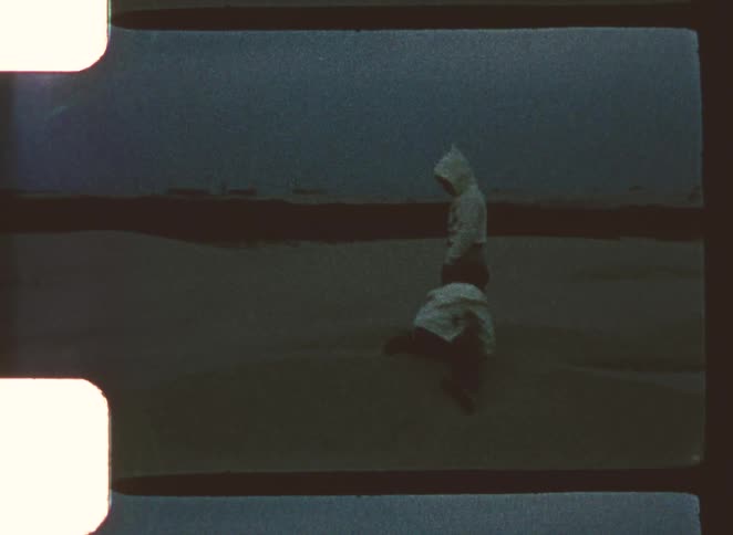 One child is crawling toward another standing child who is wearing a hood all set on a dark open landscape