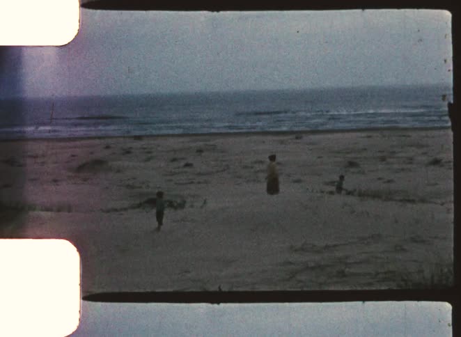 Three kids walking across the beach sand on a cloudy day