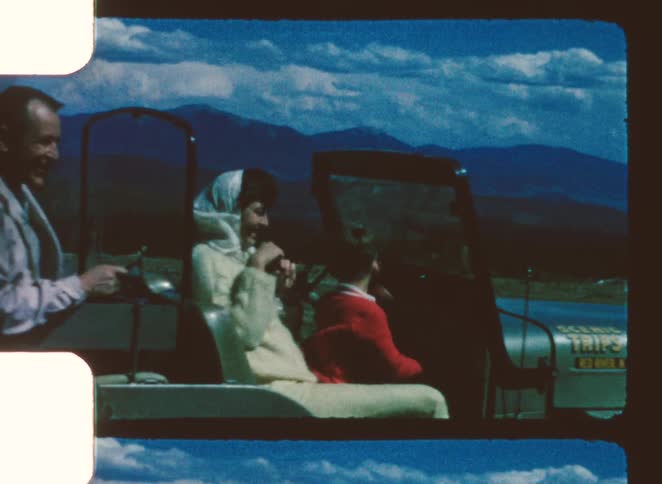 Three people seated in an open vehicle in front of a mountainous landscape