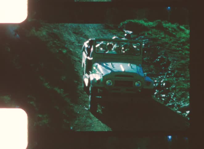 An open top jeep filled with people slowly backs up a dirt slope