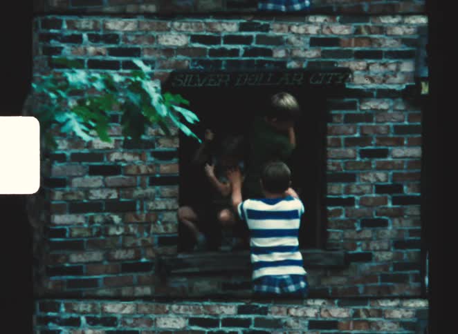 Children interacting through an opening in a brick wall in an outdoor area