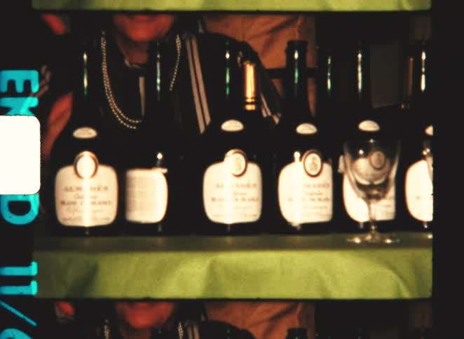 A woman sitting behind a table filled with bottles of wine smiling as she looks over the scene