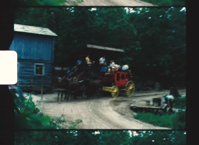 Horsedrawn carriage carrying people on a rural road beside wooden buildings