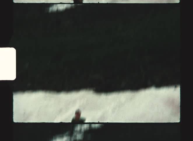A low angle vintage film view shows a man standing in a slope covered in snow throwing a snow ball up
