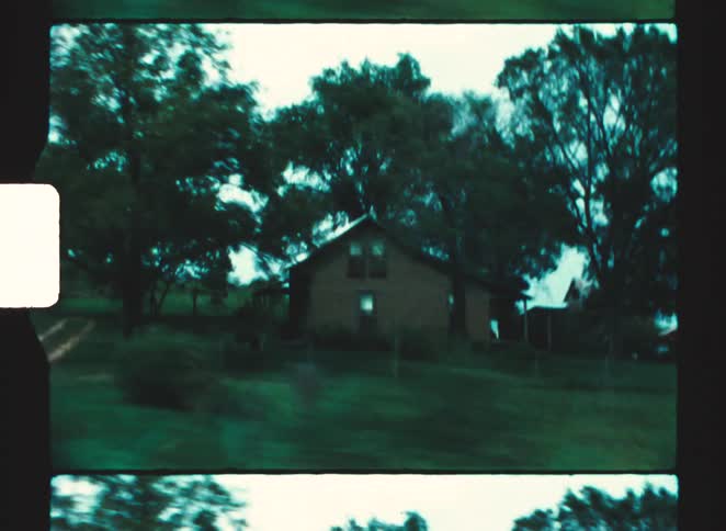 Rustic house surrounded by trees and greenery sits in rural setting with dirt path in front