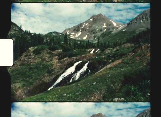 A mountain valley with evergreen forests and a cascading waterfall under blue sky