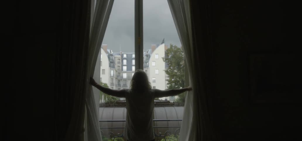 A woman opens curtains and looks out the window