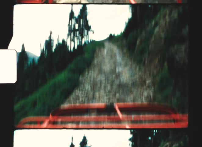 An orange vehicle is traveling on a rough rocky mountain path surrounded by a dense forest