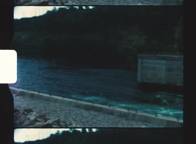 Turbulent water flows beside concrete structure with railing on sloped embankment