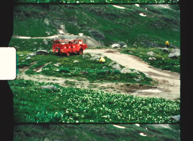A bright red off road vehicle parked on a dirt path in green mountains