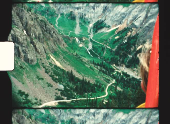 Person in yellow jacket looks at winding road in mountainous valley filled with trees and rocks