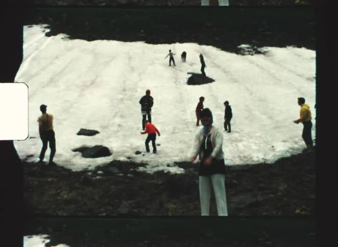 Group of people explores snowy slope with exposed rocks in a mountainous outdoor setting