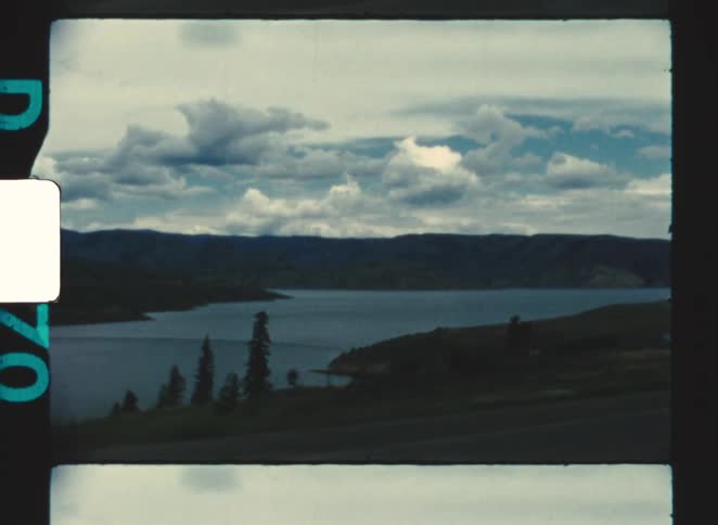 Landscape with lake surrounded by hills and mountains under dramatic sky with clouds and trees