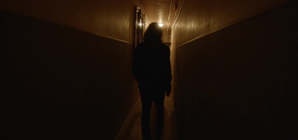 A man and woman walk down a narrow dark hallway