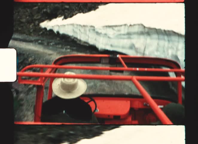 Red vehicle drives along a mountain road with snow on the right side